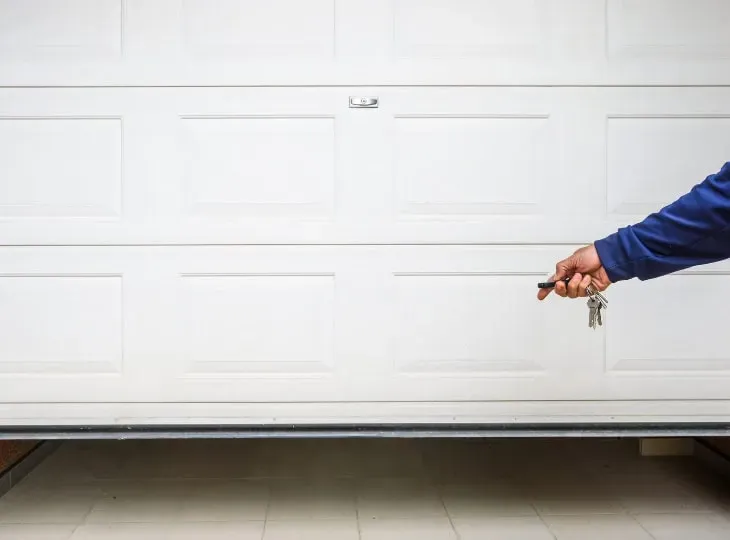 Man holding keys near a closed garage door on a bright day while preparing to park a vehicle